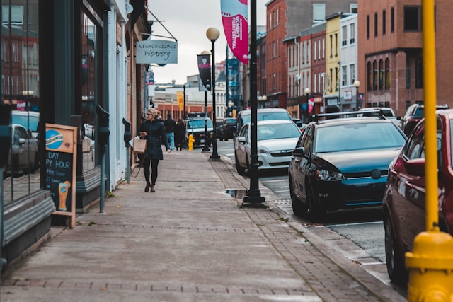 people walking on pathway near buildings and different vehicles on road during daytime